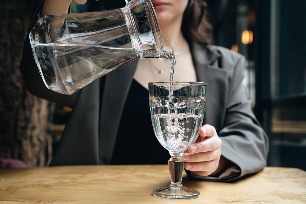 Woman pouring pure water into glass at restaurant using Sublime Environmental ozone treatment system for premium dining experience