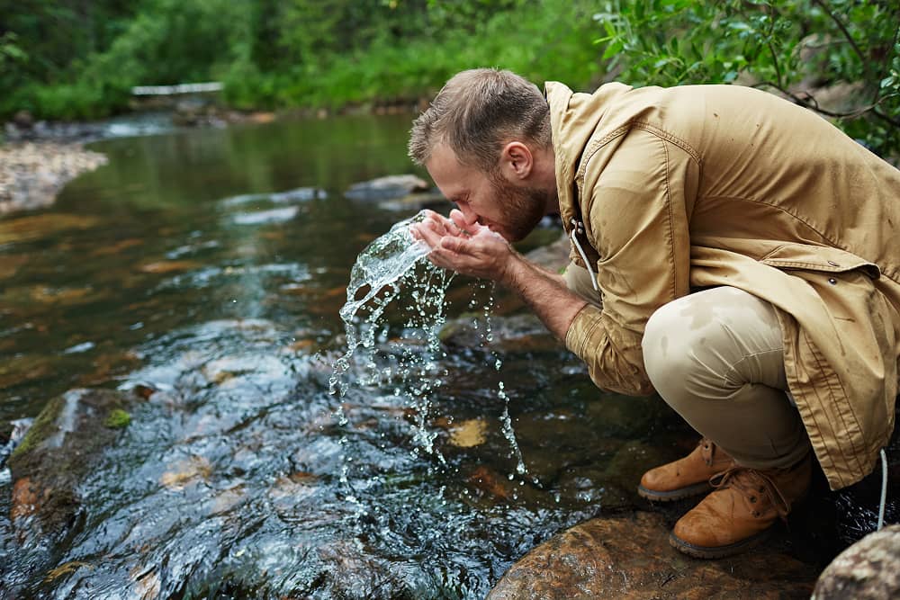 Man collecting water sample from natural water source for mining water treatment analysis